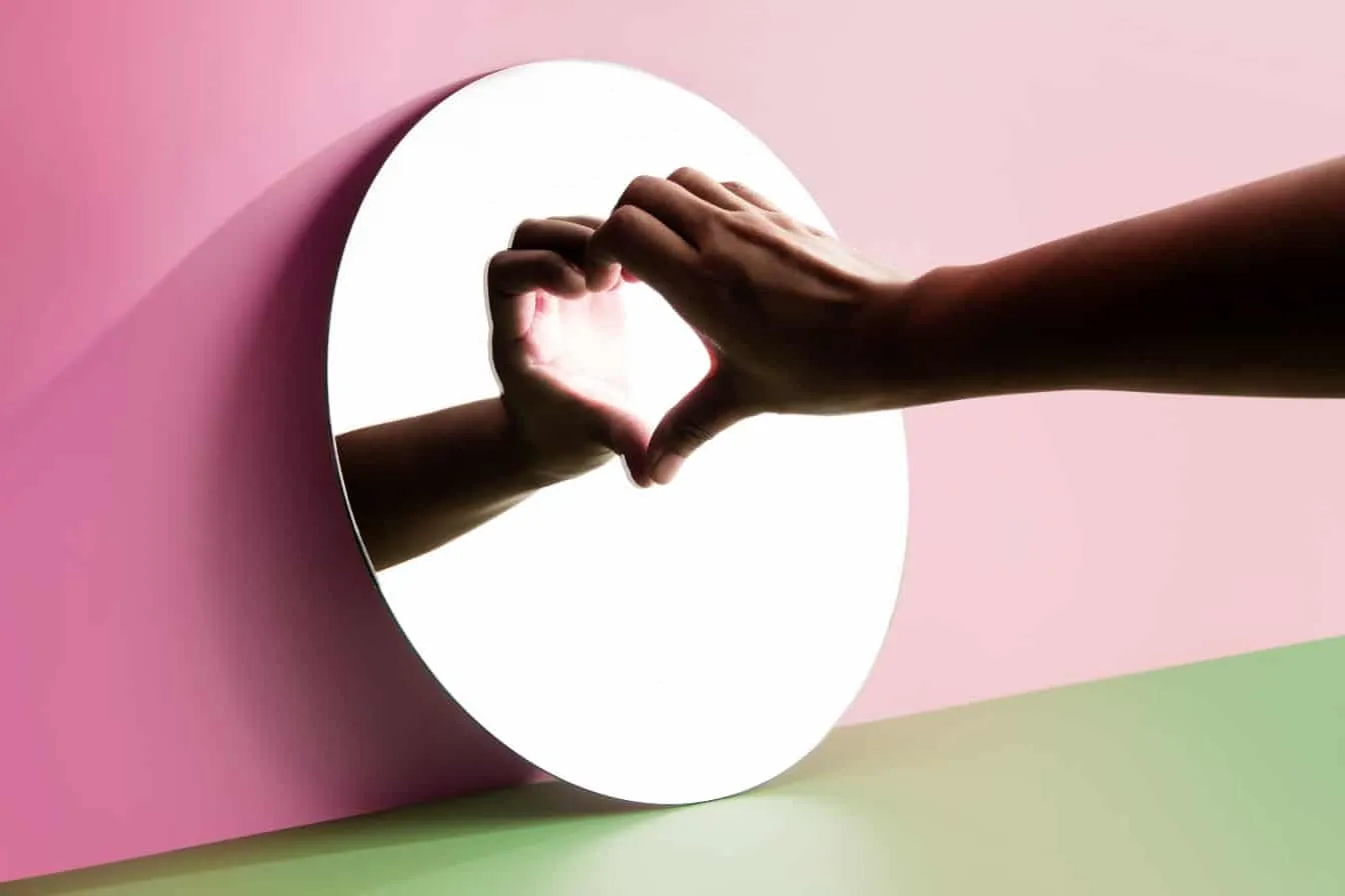 Femme faisant un cœur avec sa main sur un miroir pour montrer la souffrance du célibat