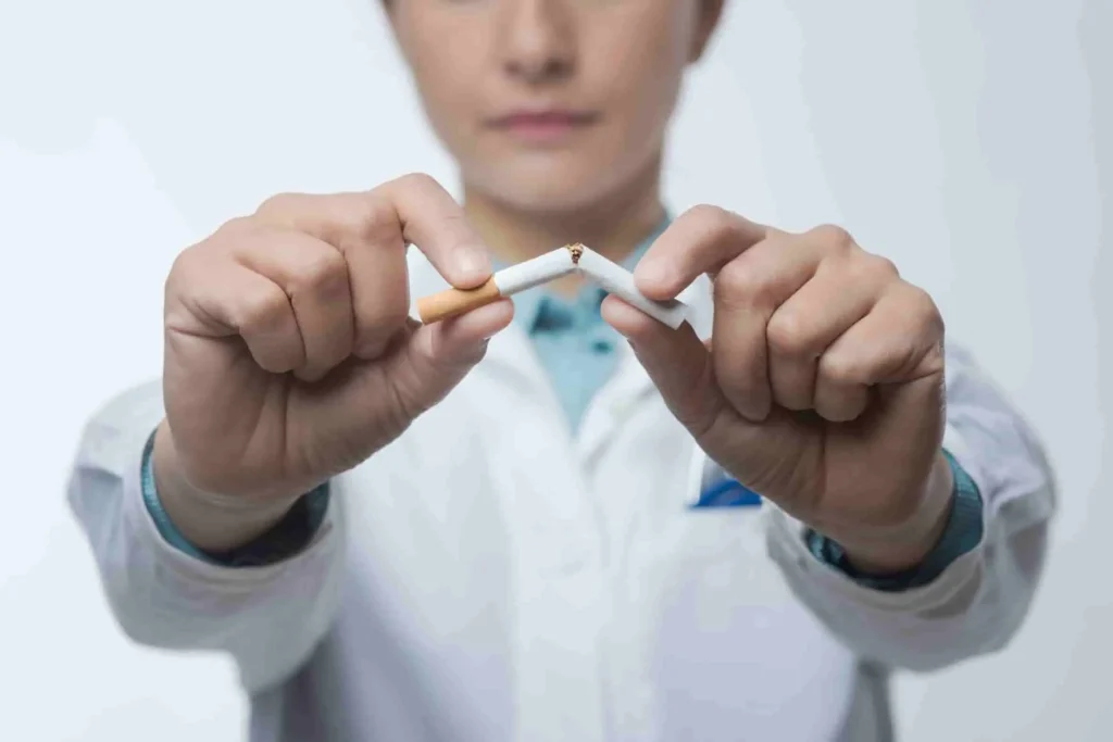 Personne en blouse blanche tenant une cigarette cassée, symbole d’arrêt du tabac pour préserver la santé pulmonaire et prévenir les nodules aux poumons.