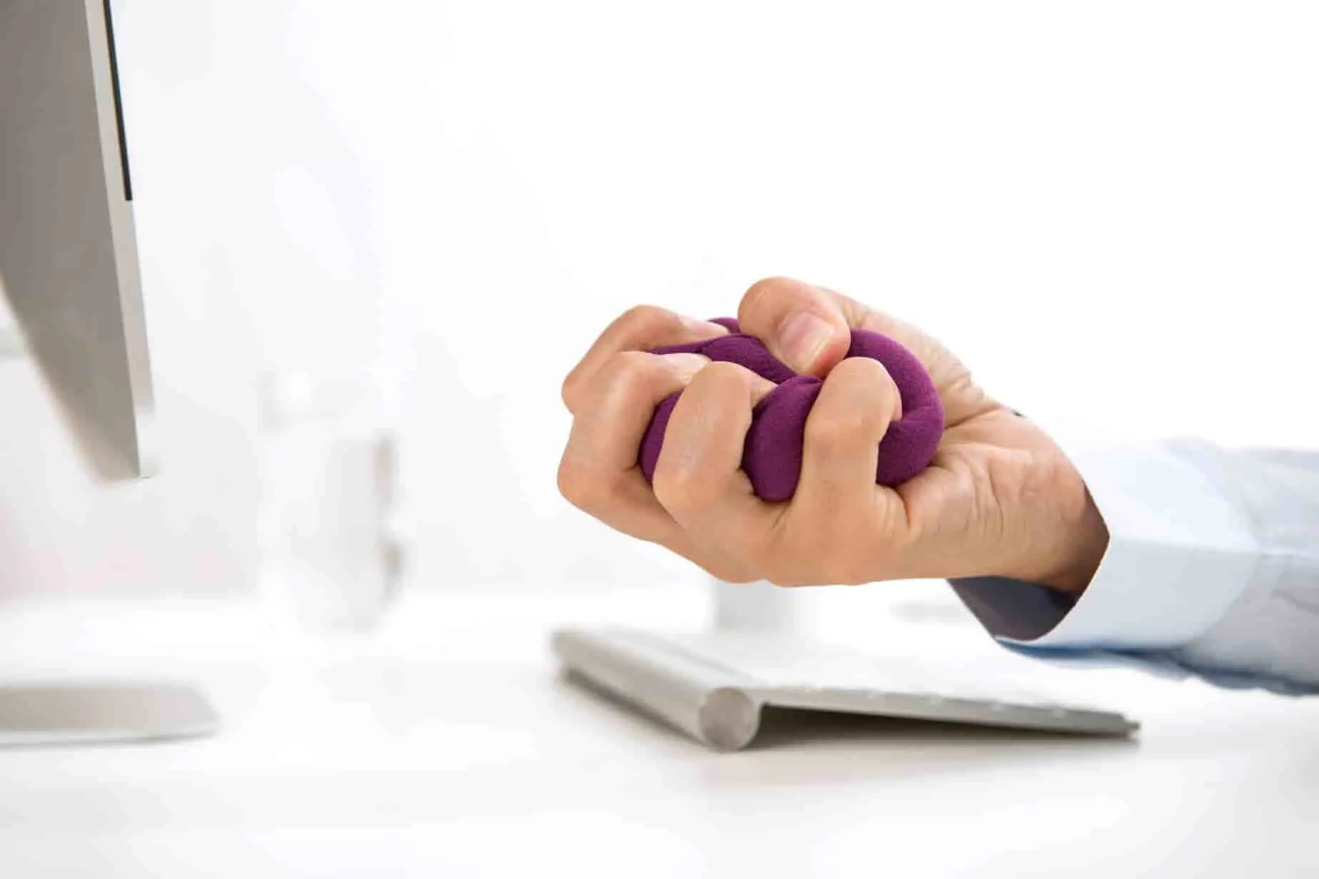 Main serrant une balle anti-stress violette devant un écran, image qui évoque un exercice ciblé pour affiner les doigts dans un contexte de tension