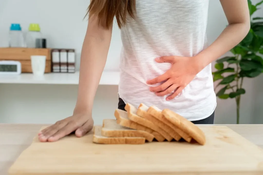 Personne en cuisine tenant son ventre devant des tranches de pain illustrant un inconfort lié à la maltodextrine