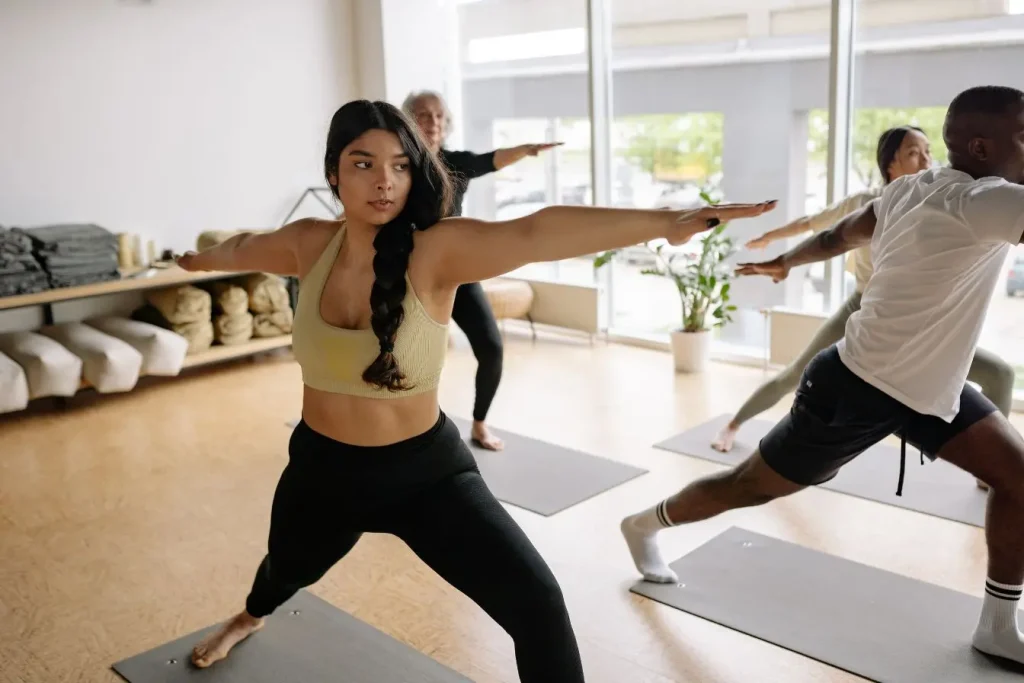 Groupe en studio lumineux pratiquant posture du guerrier II, image illustrant exercices pour améliorer la posture et renforcer l’alignement corporel.