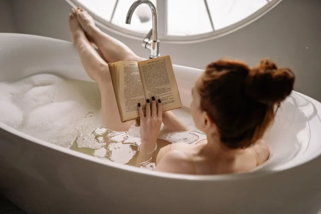 Personne détendue dans une baignoire avec livre, image illustrant les bienfaits du bain froid pour stimuler la circulation et apaiser le corps.