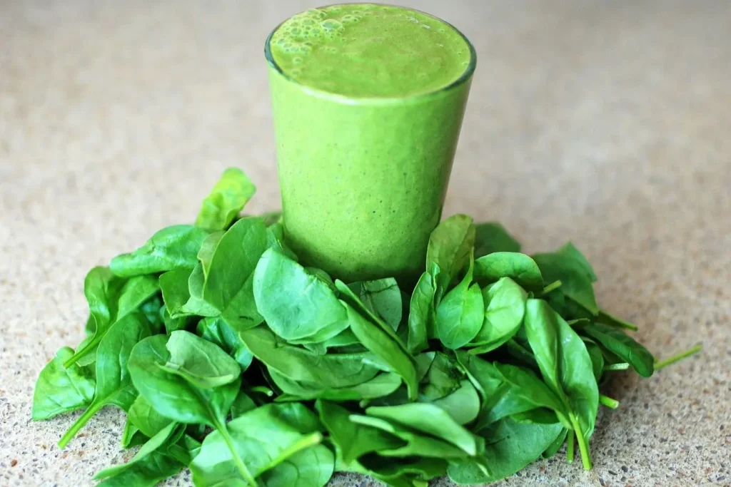 Verre de smoothie vert posé sur plan de travail entouré de feuilles fraîches, image illustrant la posologie idéale de la chlorella en boisson santé quotidienne.