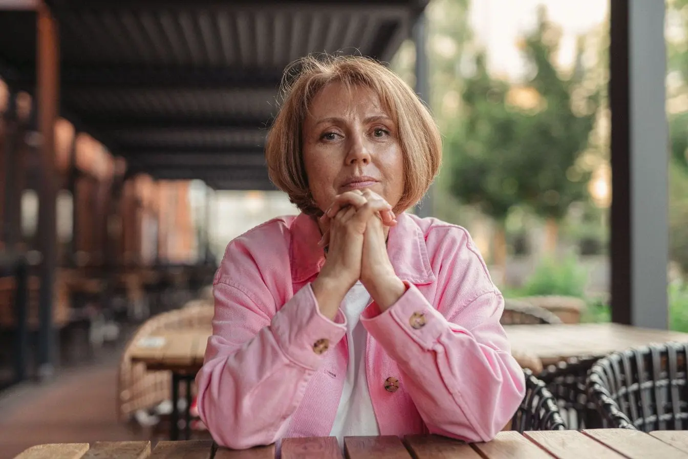 Femme assise en extérieur Femme posée dans un café, attitude pensive qui reflète les interrogations autour de la ménopause précoce et ses impacts.