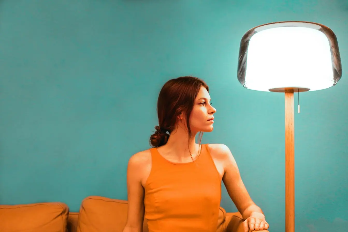 Personne assise sur canapé coloré près d’une lampe allumée, image illustrant l’usage de la luminothérapie pour soulager la dépression saisonnière.