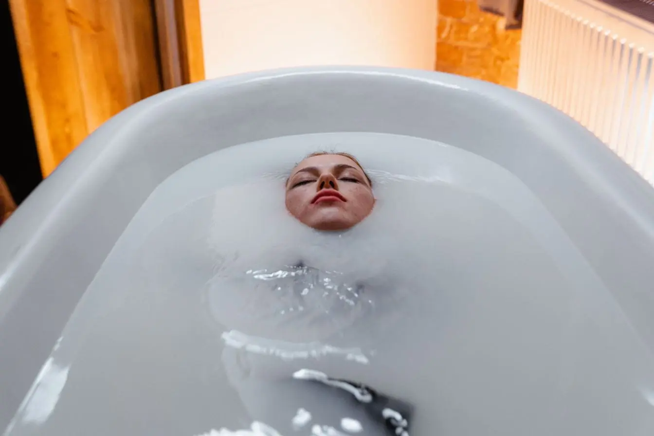 Personne allongée dans baignoire remplie d’eau opaque, image illustrant une séance de cryothérapie corps entier.