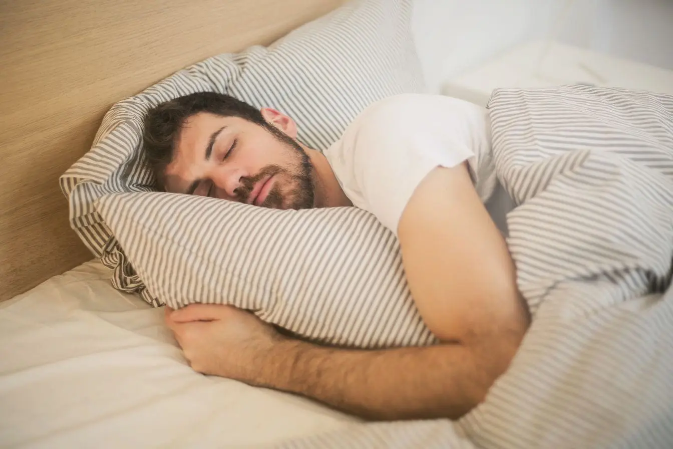 Personne dormant paisiblement sous couverture rayée Personne dormant paisiblement sous couverture rayée, image qui illustre les méthodes naturelles pour réduire le ronflement et améliorer le sommeil.