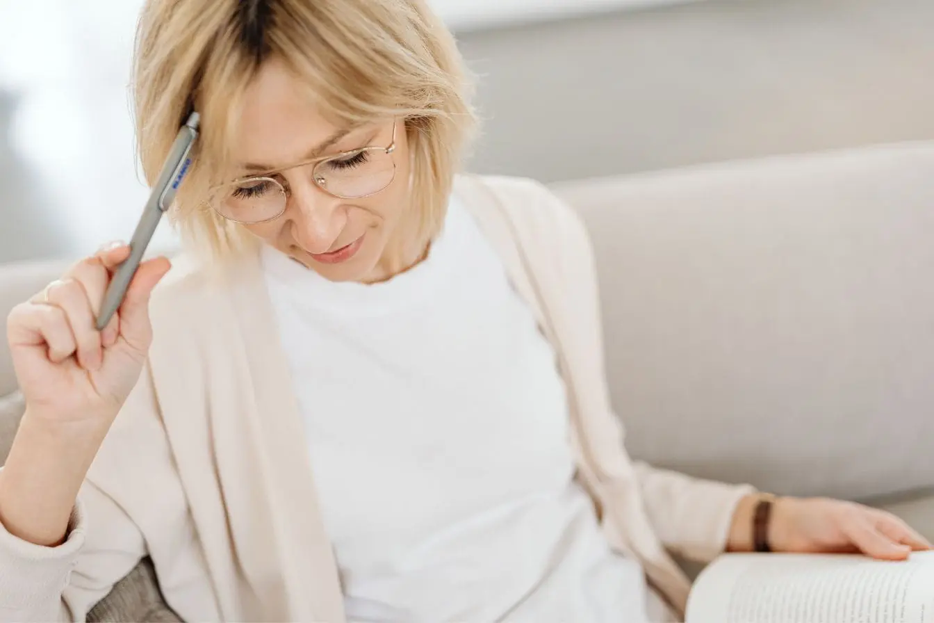 TDAH adulte Personne assise sur canapé avec livre ouvert et stylo, image qui illustre la difficulté de concentration liée au TDAH chez l’adulte.