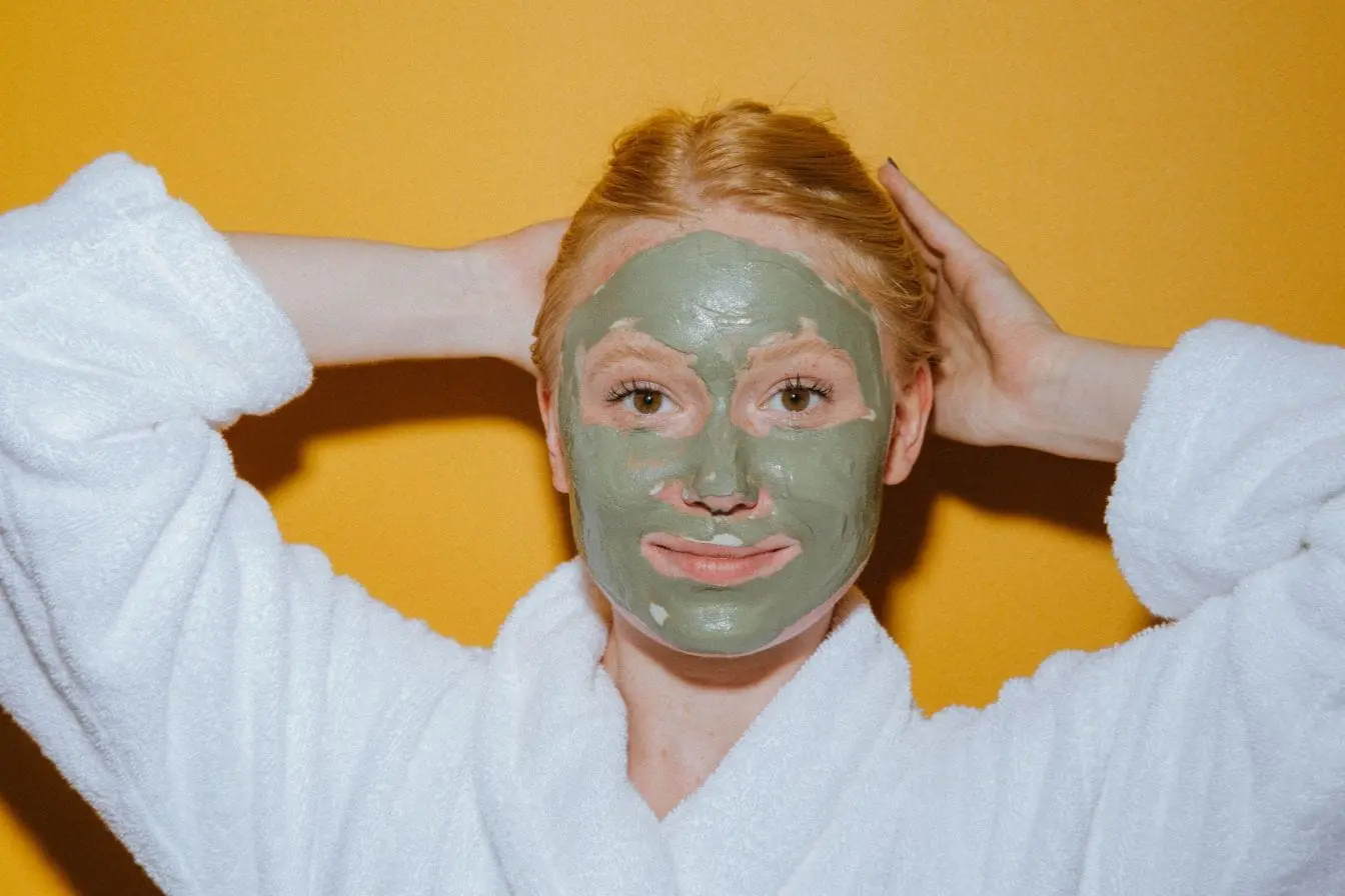 argile verte Personne en peignoir blanc avec masque vert sur le visage, image qui illustre les bienfaits de l’argile verte au quotidien.