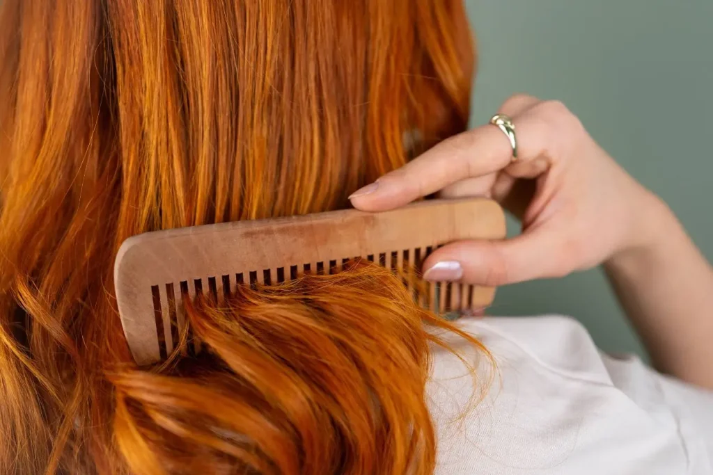 Gros plan sur une chevelure rousse peignée avec un peigne en bois, image qui illustre l’usage quotidien de l’argile verte pour renforcer et purifier les cheveux.