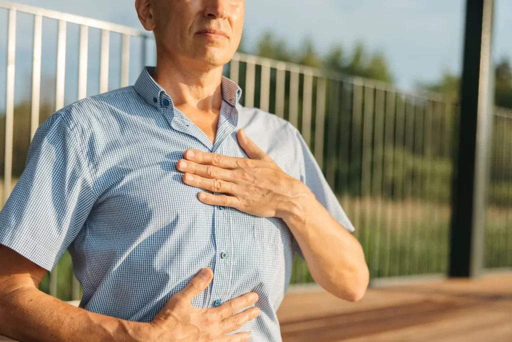 Personne en chemise bleue place une main sur poitrine et l’autre sur ventre, image illustrant un exercice de respiration lié à la cohérence cardiaque.