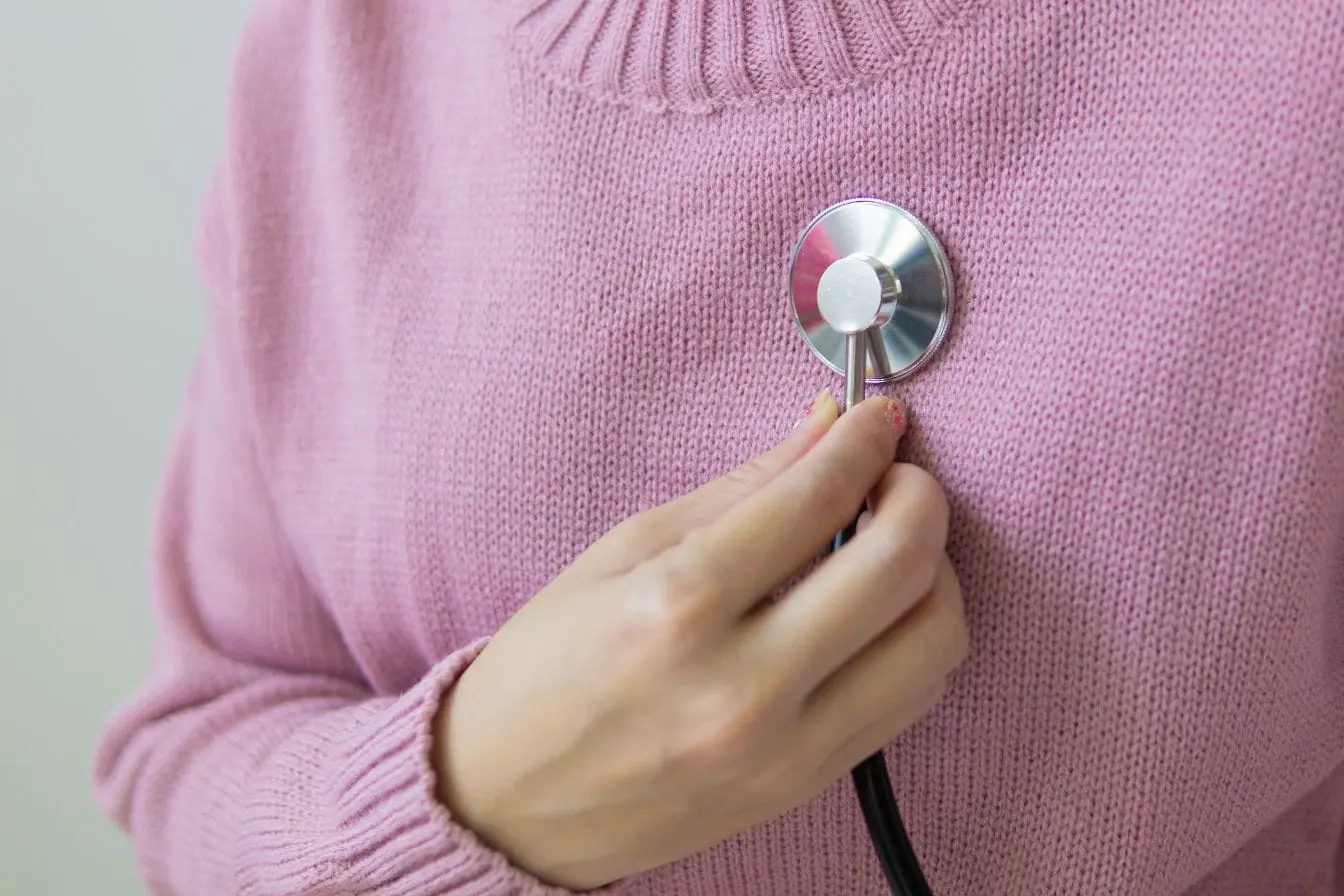 Personne en pull rose tient stéthoscope sur poitrine, image illustrant une pratique liée à la cohérence cardiaque.