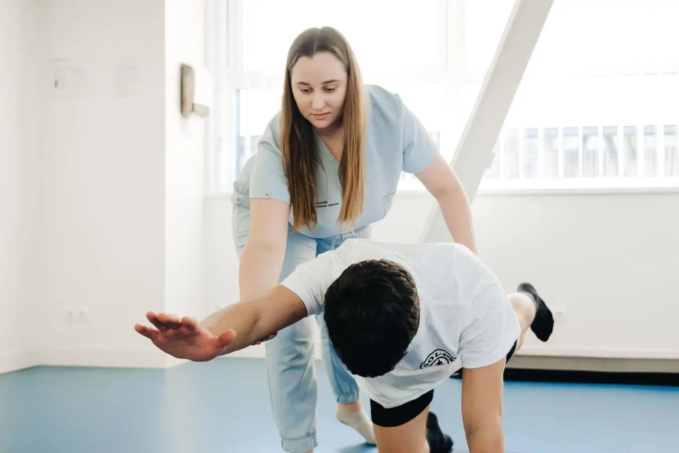 soulager un psoas Patient guidé par un kinésithérapeute en tenue bleue, effectuant un exercice au sol pour soulager un psoas contracté dans une salle lumineuse.