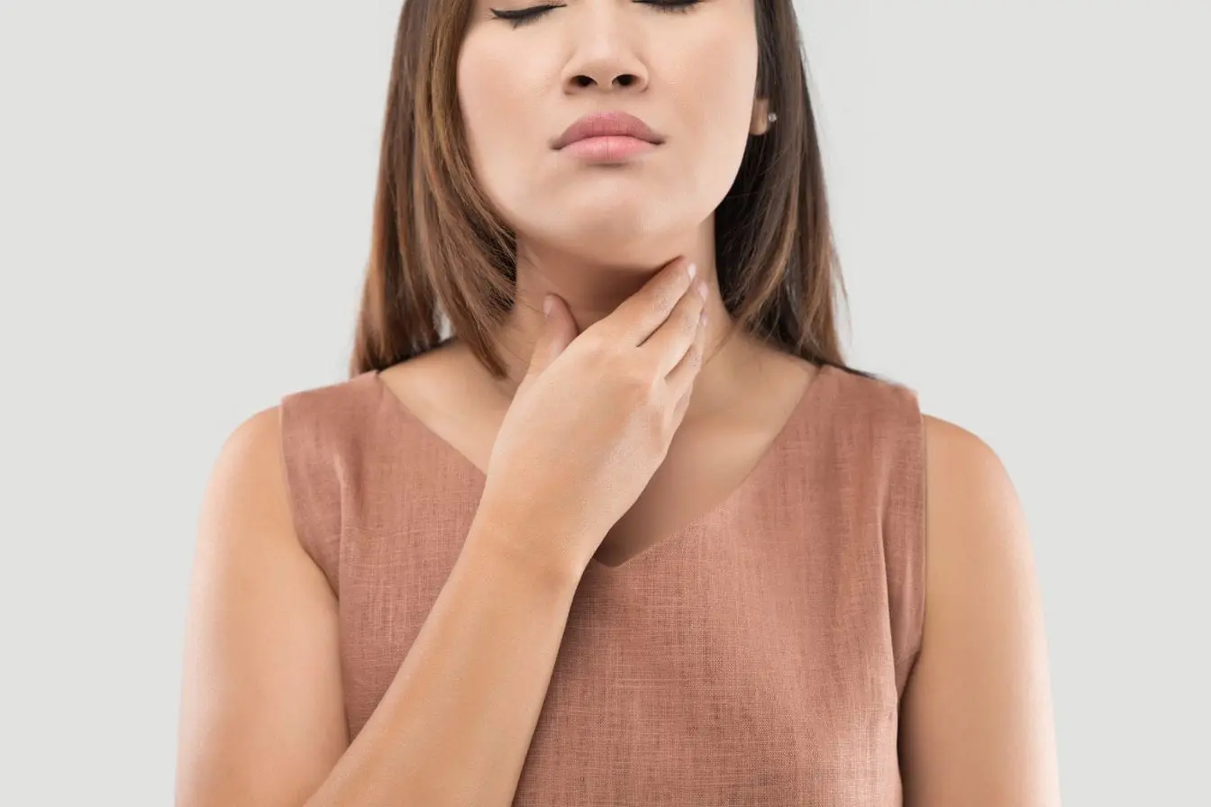 thyroïdite de Hashimoto Personne en haut gris pose main sur gorge yeux fermés, image illustrant les impacts alimentaires liés à la thyroïdite de Hashimoto.