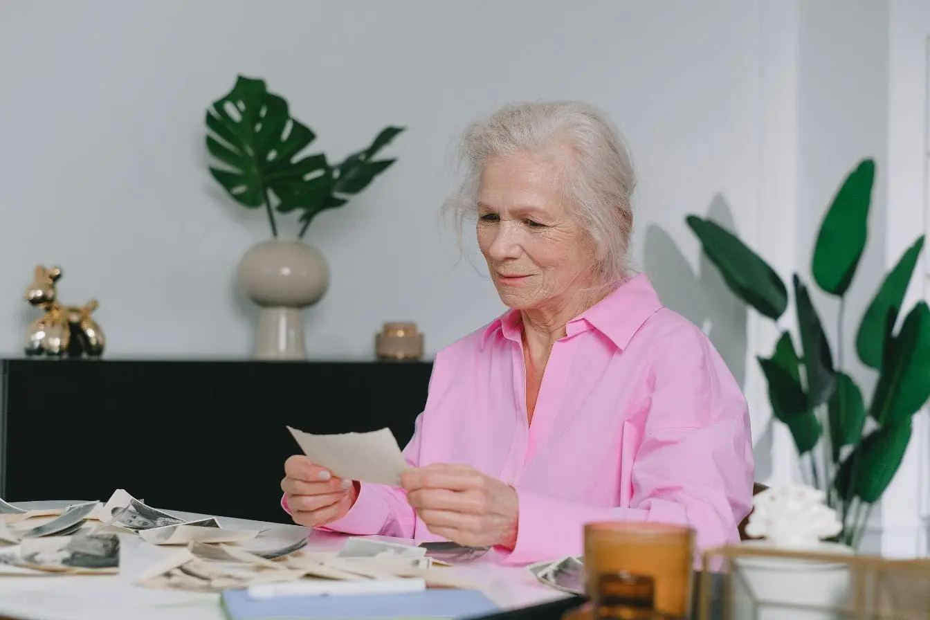 Personne âgée Personne âgée en chemise rose observant photos anciennes, image qui illustre la stimulation de la mémoire pour réduire le risque d’Alzheimer naturellement.