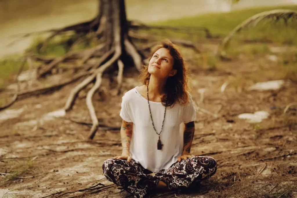 Personne assise en tailleur près d’un grand arbre, image qui illustre les bienfaits du grounding pour se reconnecter à la terre et apaiser l’esprit.