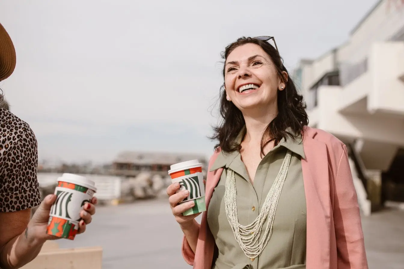 Scène urbaine avec deux femmes Deux personnes détendues tenant des cafés festifs en extérieur, image qui illustre un moment convivial associé à l’équilibre hormonal naturel.
