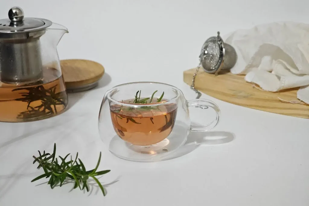 Tasse de tisane aux herbes avec romarin flottant, image qui illustre un remède naturel efficace contre les mains froides.