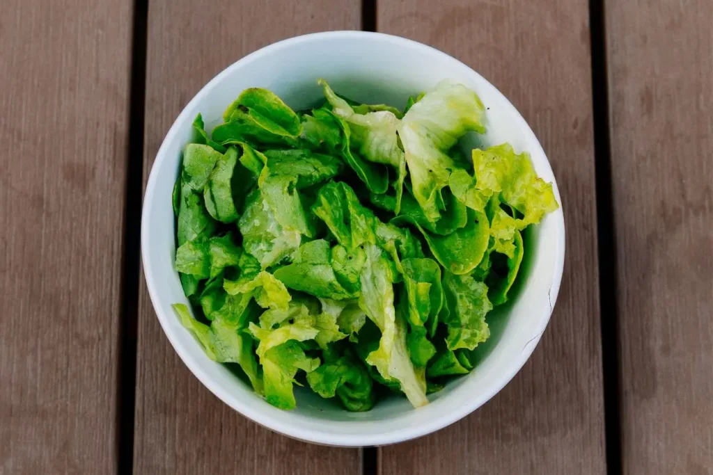 Bol blanc rempli de feuilles de laitue fraîches sur bois, image qui illustre l’importance d’une alimentation anti-acné pour une peau plus nette.