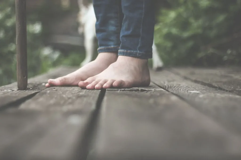 Personne en jeans debout pieds nus, image qui traduit le geste simple et authentique de marcher pieds nus.