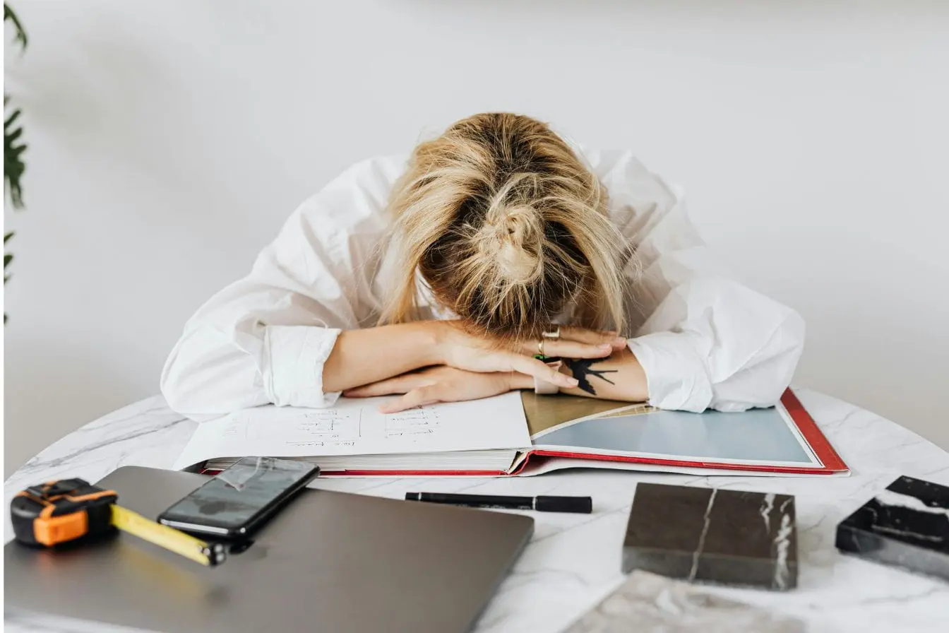 syndrome de fatigue chronique Personne en chemise blanche la tête posée sur ses bras, image qui illustre l’épuisement lié au syndrome de fatigue chronique.
