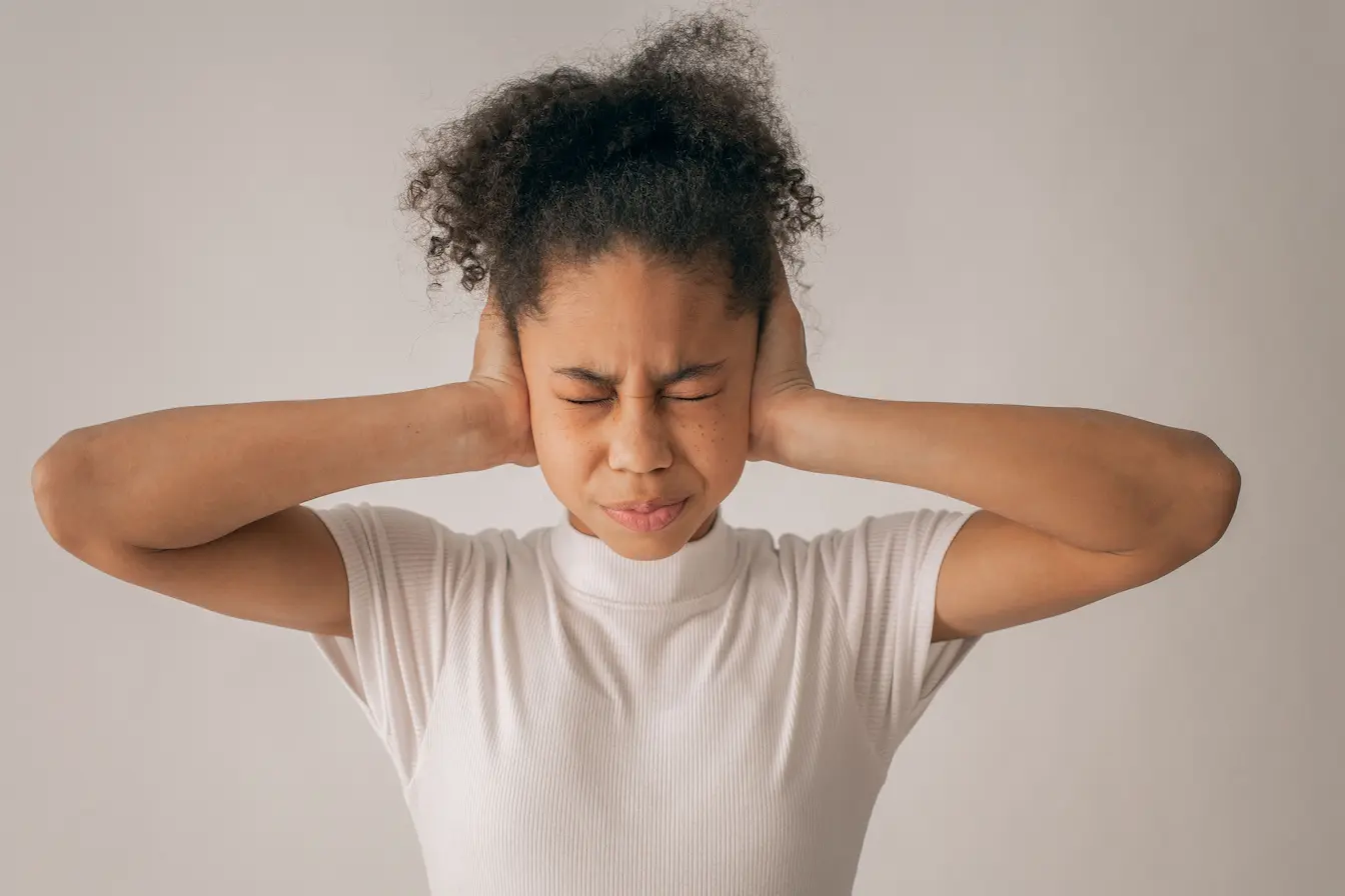 Personne en chemise blanche pressant ses oreilles Personne les mains sur les oreilles et yeux fermés, image qui illustre la recherche de solutions pour soulager les acouphènes.