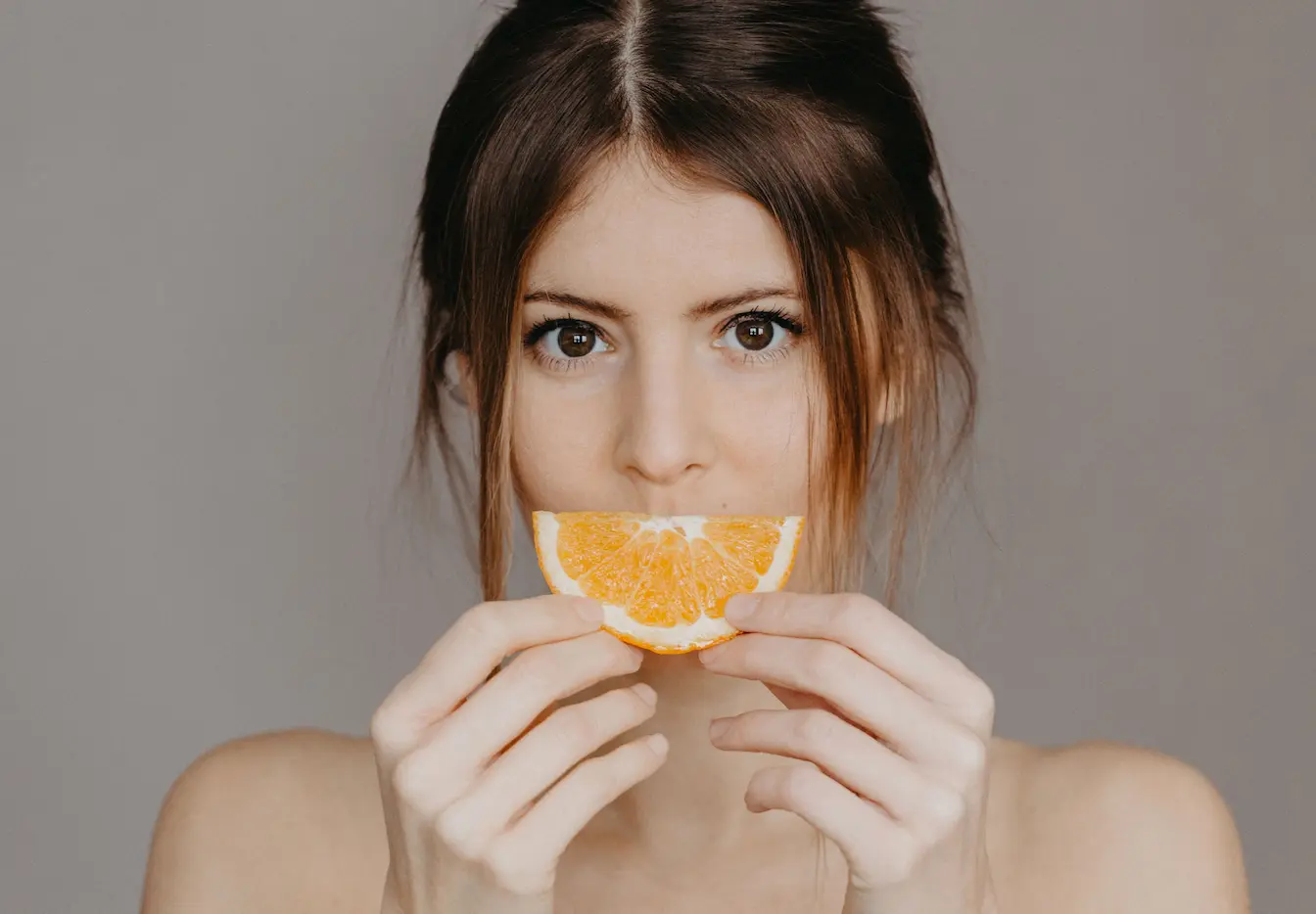 Personne tenant une tranche d’orange Personne tenant une tranche d’orange devant sa bouche, image qui illustre la carence en vitamine D.