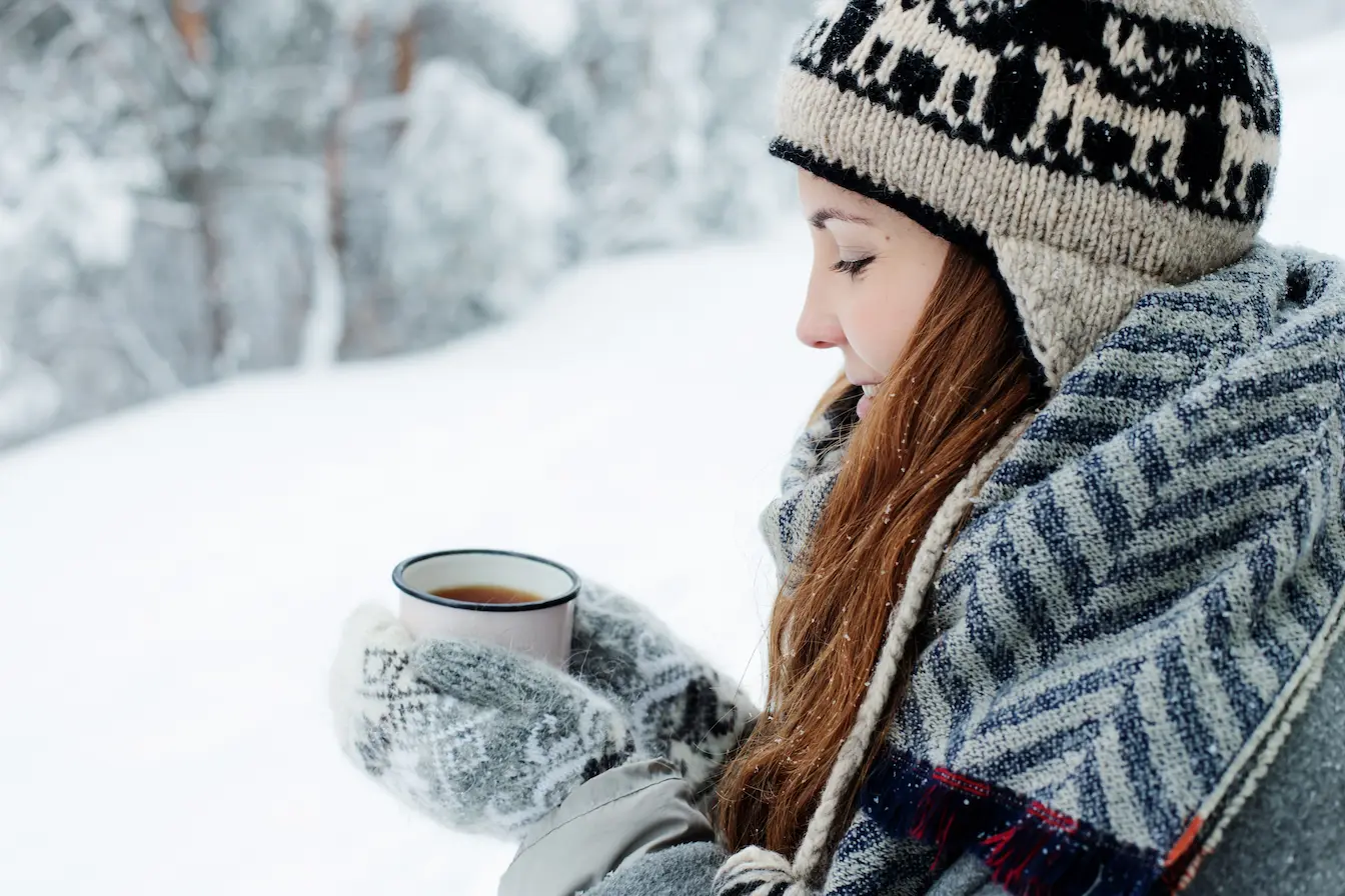 Scène enneigée Personne emmitouflée en bonnet et écharpe tenant boisson chaude, geste reflétant les moyens naturels pour renforcer son système immunitaire en hiver.