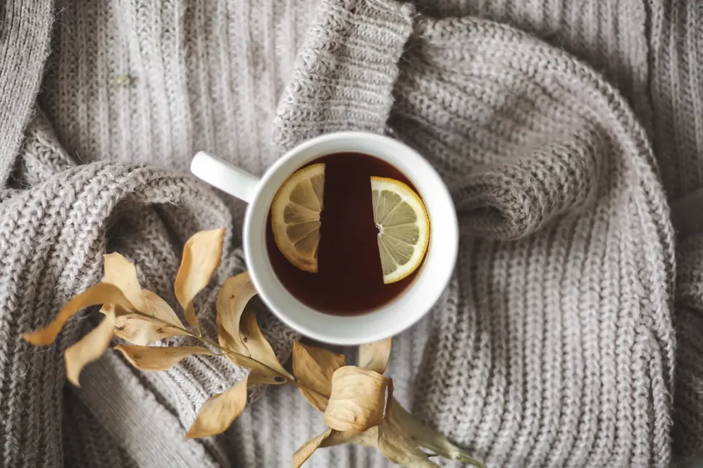 Tasse de thé chaud au citron posée sur tissu gris, symbole des gestes naturels pour renforcer son système immunitaire en hiver.