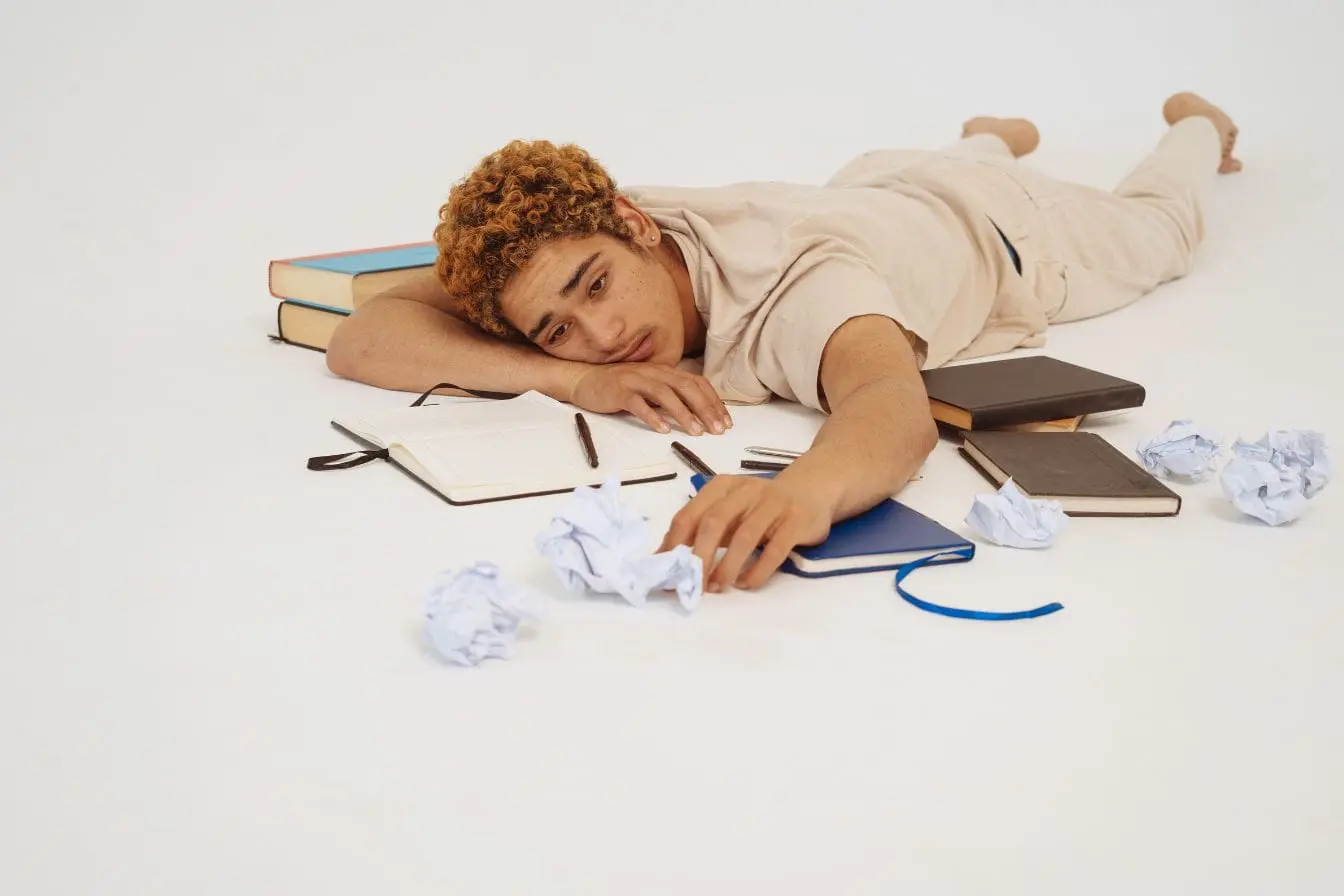 burn‑out Personne allongée face contre bureau entourée de papiers froissés, reflet des signes de burn‑out distincts de la dépression.