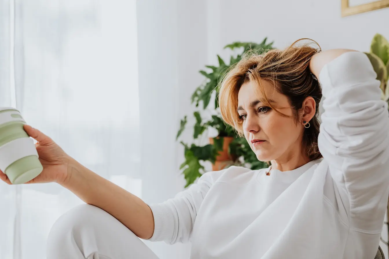 femme en sweat blanc Gros plan sur femme assise touchant ses cheveux, reflet des bouffées de chaleur hors ménopause et des origines variées.