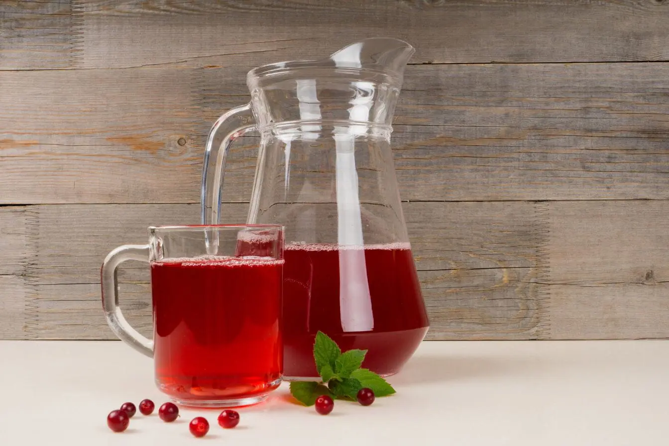 jus de cranberry Carafe et tasse de jus rouge entourées de baies, reflet d’un traitement naturel pour soulager la cystite interstitielle grâce aux bienfaits des fruits.