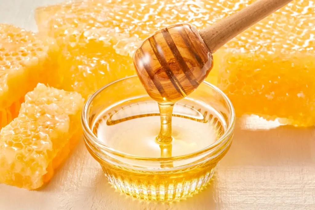 Bol transparent rempli de miel doré avec cuillère en bois, reflet des remèdes naturels souvent utilisés pour soulager les symptômes d’une rhinite allergique.