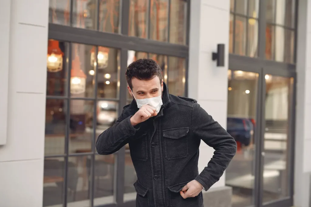 Personne masquée en extérieur levant bras pour couvrir bouche, reflet des causes possibles d’une toux sèche persistante.