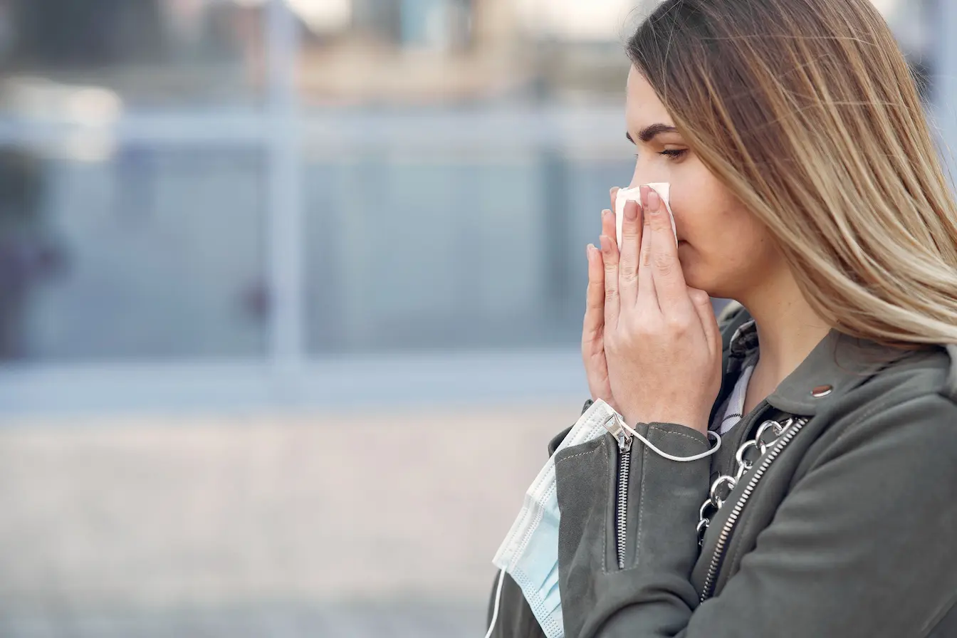 Personne en veste verte tenant mouchoir sur nez, geste reflétant les solutions naturelles pour soigner un rhume rapidement.