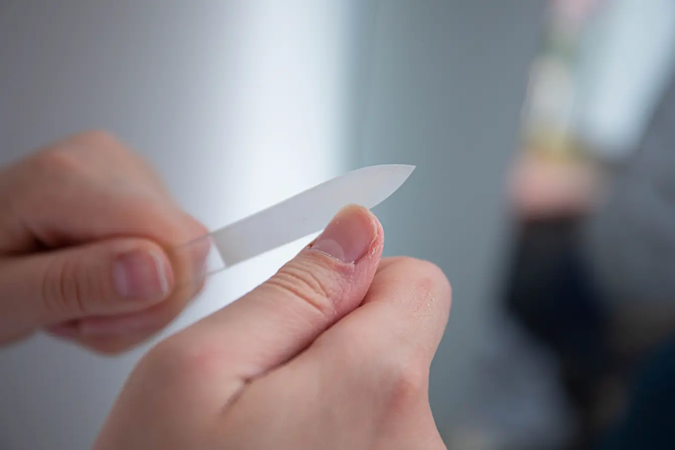 soigner une mycose des ongles Gros plan sur des mains utilisant une lime transparente pour traiter un ongle, image qui illustre le soin d’une mycose des ongles.