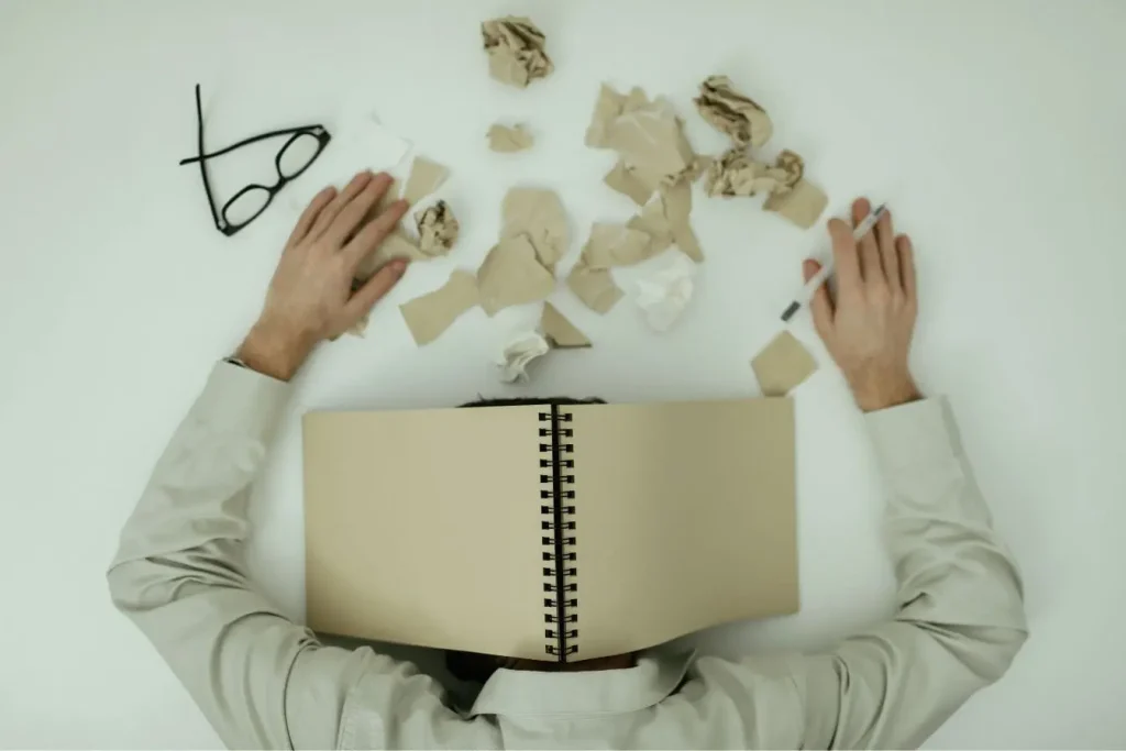 Individu la tête cachée sous carnet, illustration typique des symptômes de burn‑out.
