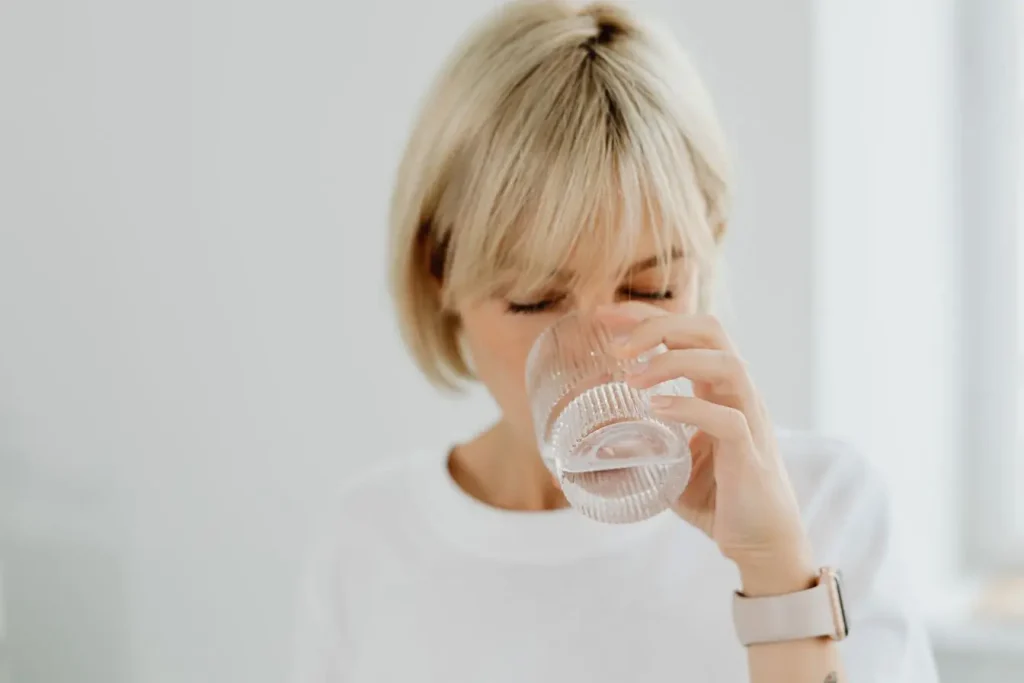 Personne en chemise blanche buvant un verre d’eau claire, symbole d’un geste simple pour retrouver de l’énergie le