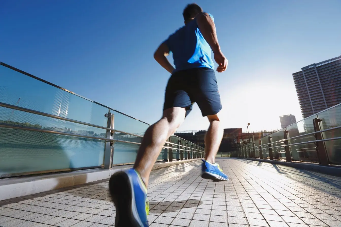 Coureur en tenue bleue Coureur en tenue bleue avançant sur passerelle urbaine ensoleillée, symbole de la motivation sportive au quotidien.