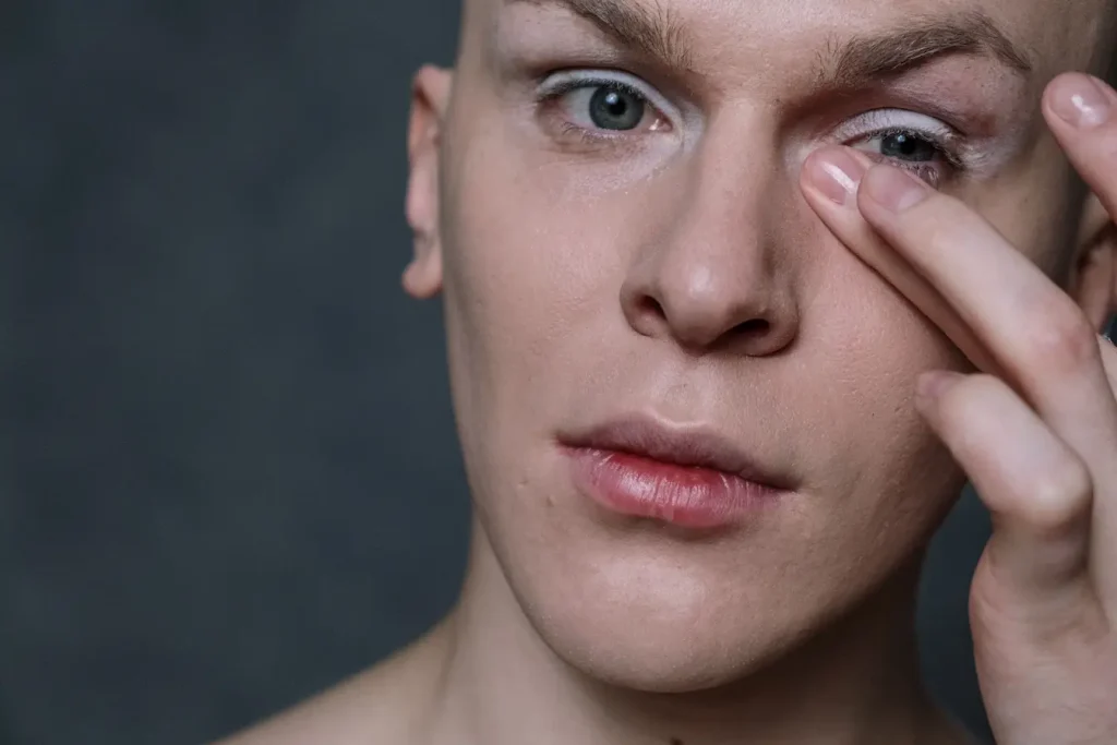 Personne au visage neutre touchant la zone près de l’œil, symbole des tremblements de paupière et de leurs causes possibles.