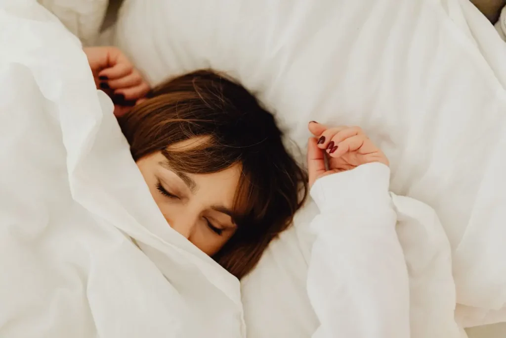 Personne allongée sous drap blanc, yeux clos et mains près du visage, symbole du repos naturel contre la fatigue chronique.