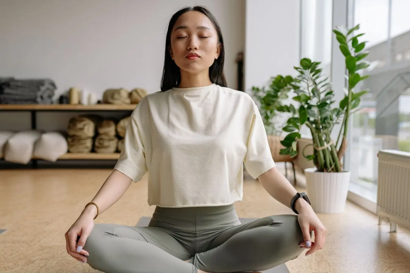 exercices de respiration Personne assise en tailleur sur tapis de yoga, yeux fermés et mains sur genoux, symbole des exercices de respiration pour s’endormir.