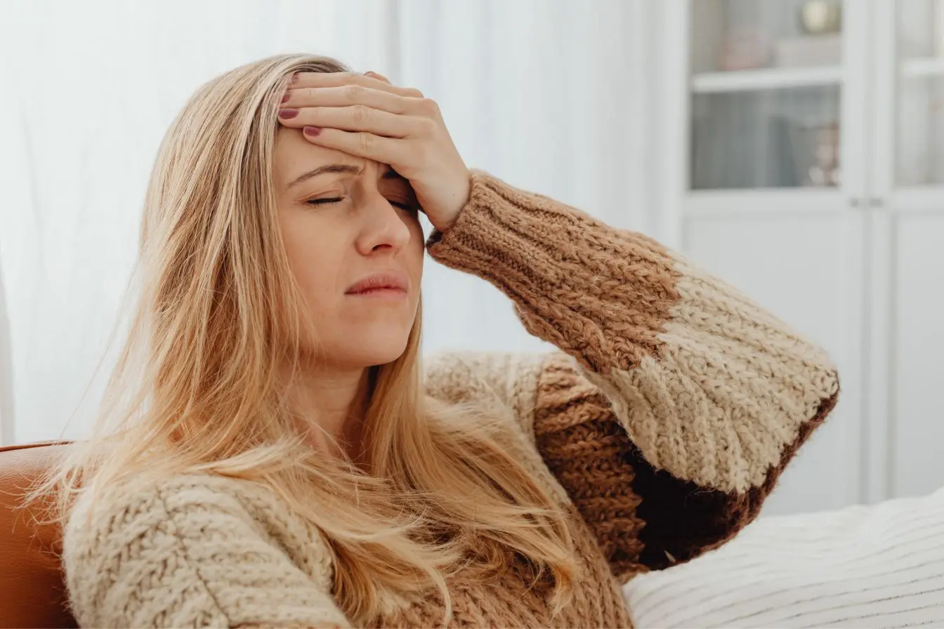 fatigue chronique Personne assise en pull tricoté beige tenant son front, symbole des effets visibles de la fatigue chronique.
