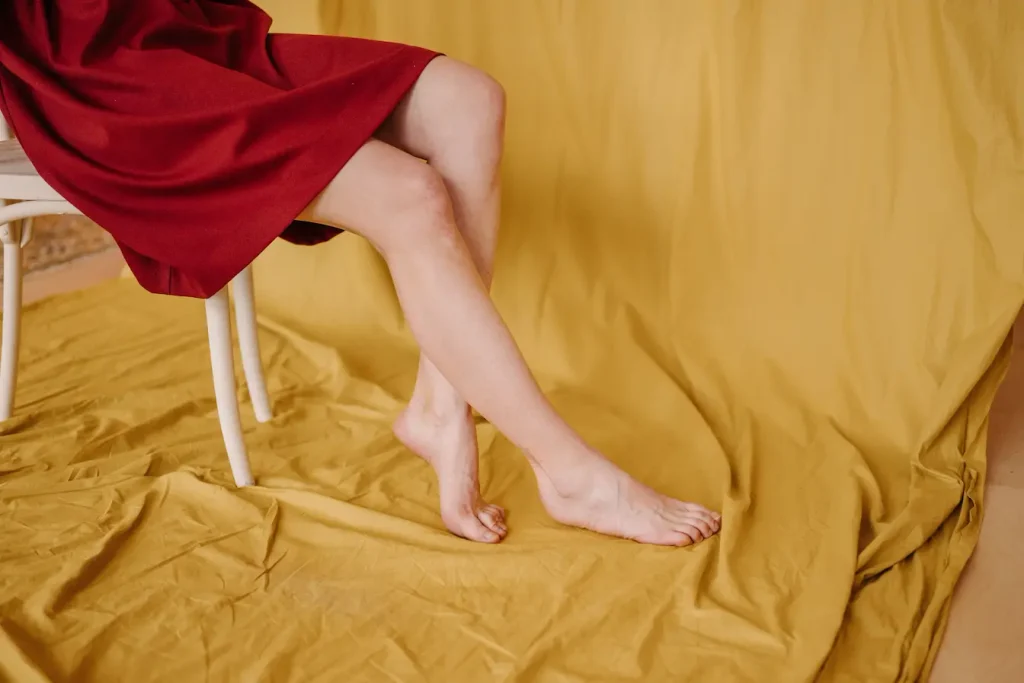 Personne assise en robe rouge avec jambes croisées, symbole des tremblements pouvant révéler un déséquilibre musculaire ou nerveux.