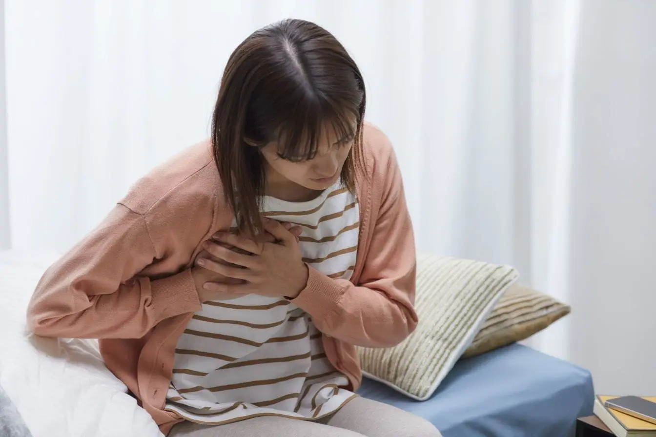 mieux respirer en cas de stress Personne assise sur lit tenant sa poitrine, symbole des gestes liés aux exercices de respiration pour apaiser le stress.