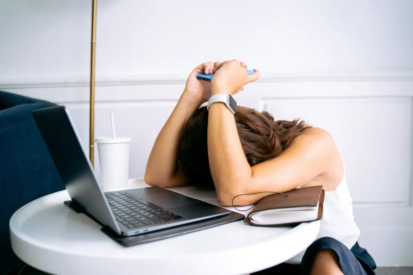 procrastiner Une femme découragée baisse la tête sur son bureau entre un ordinateur portable et un carnet en cherchant la motivation pour enfin avancer.