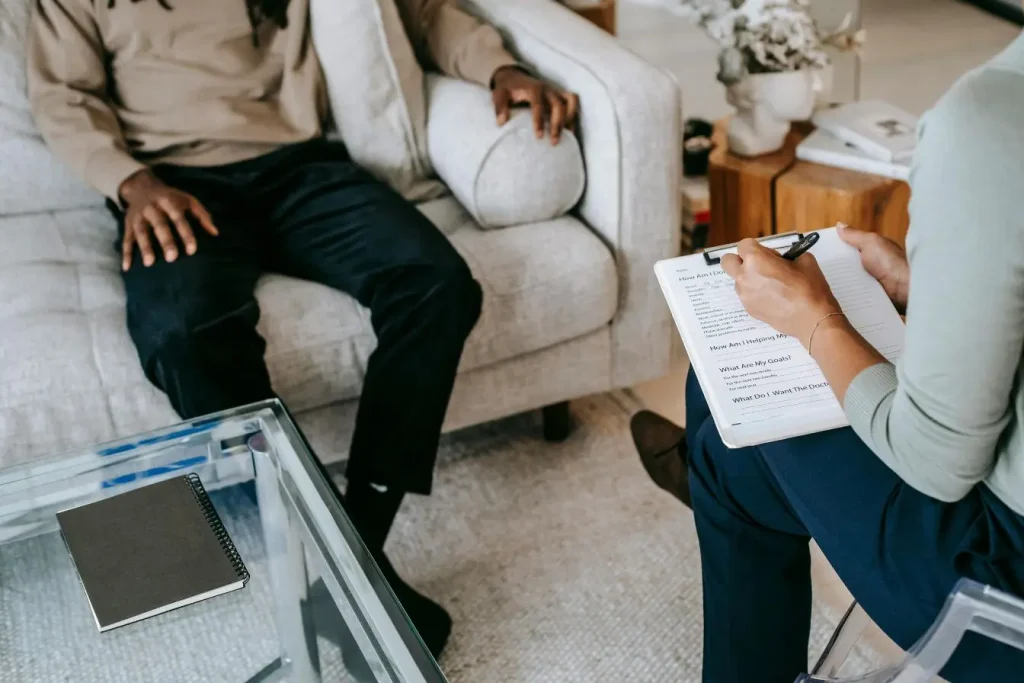 Une personne assise sur un canapé en consultation avec un thérapeute qui prend des notes, illustrant l'accompagnement pour reconnaître un trouble de l'attachement.