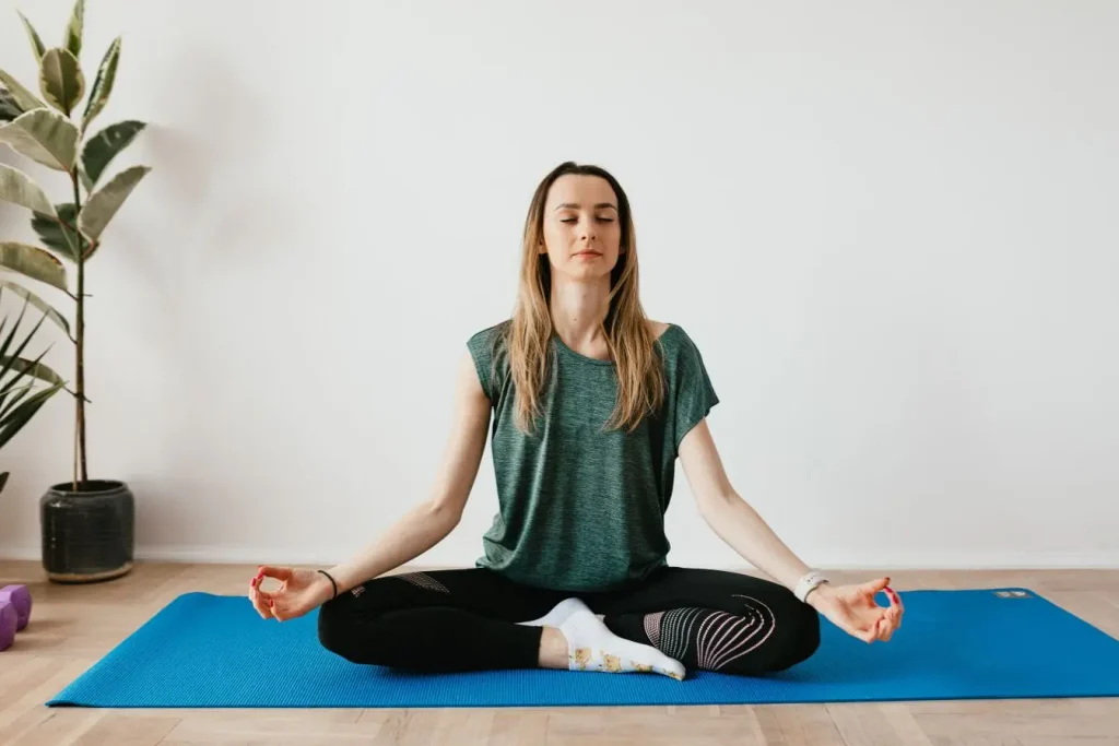 Personne assise en tailleur sur tapis bleu, yeux fermés et mains sur genoux, symbole des exercices de respiration pour apaiser le stress.