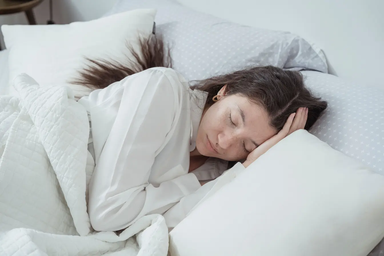 soulager un torticolis en dormant Personne allongée sur le côté avec tête posée sur oreiller blanc, symbole des positions de sommeil pour soulager un torticolis.