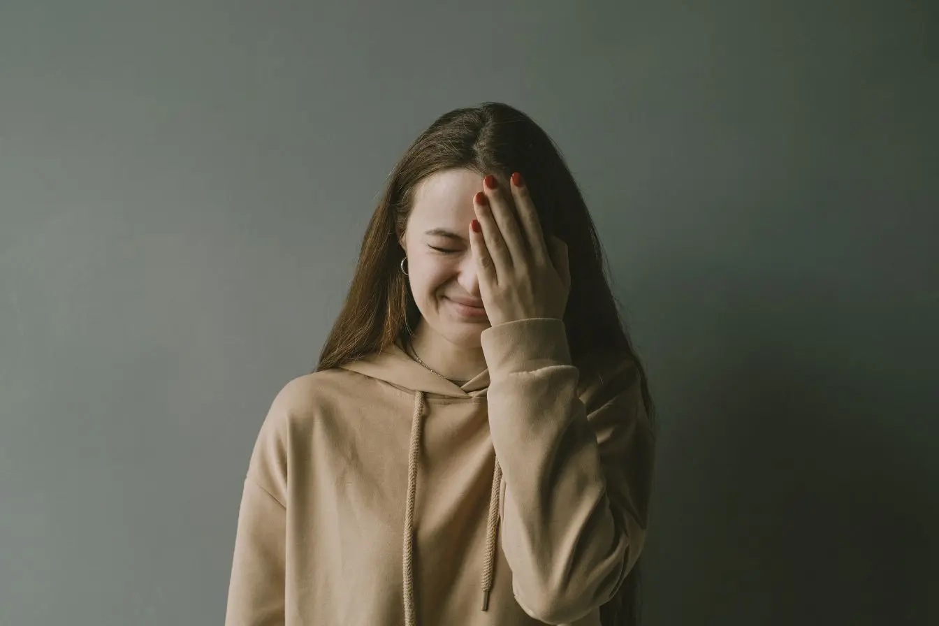Une jeune femme portant un sweat à capuche beige se cachant le visage de la main, idéale pour illustrer la détresse et reconnaître un trouble de l'attachement.